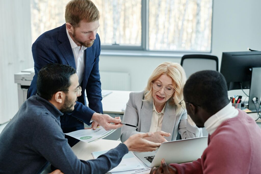 A diverse group of professionals engaged in a collaborative office meeting with laptops and documents.